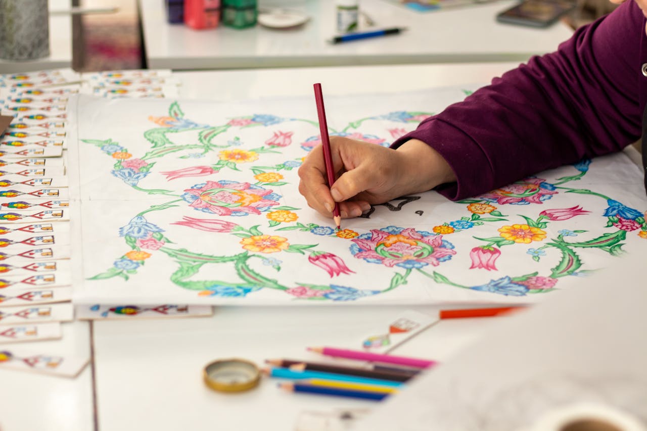 A person coloring a detailed floral design with pencils, showcasing creativity.