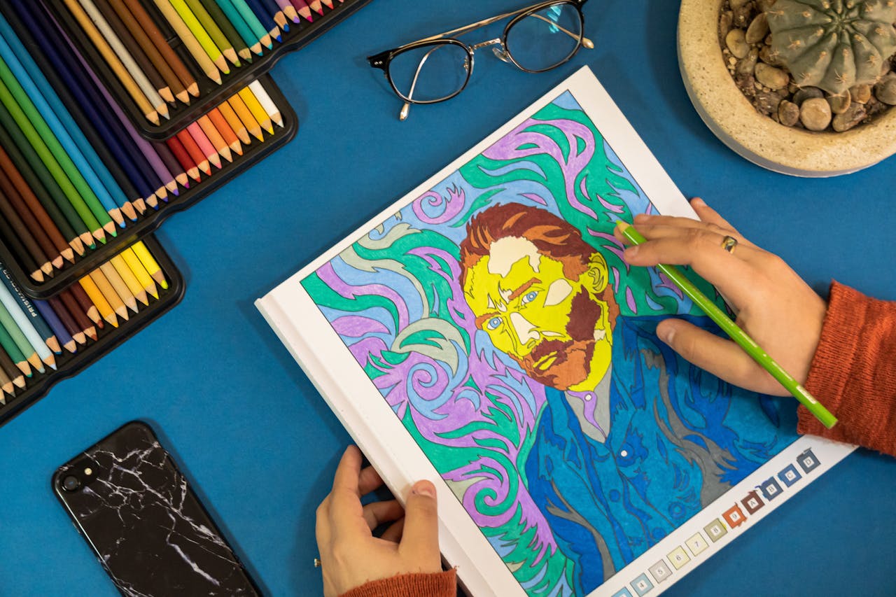 Hands coloring a Van Gogh artwork with vibrant pencils on a blue workspace.