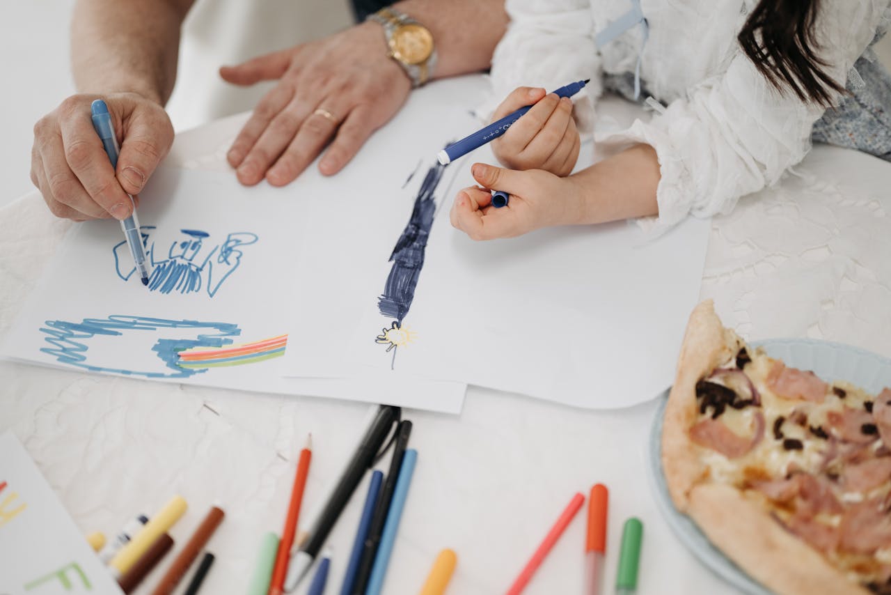 A child and adult drawing together with markers and paper, sharing creativity.